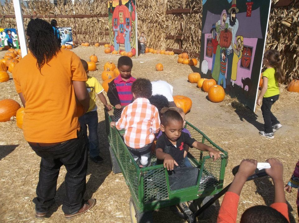 A group of children are riding in a wagon at a pumpkin patch.