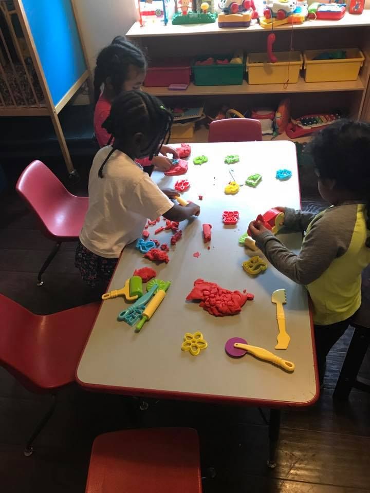 Three children are playing with play dough at a table.