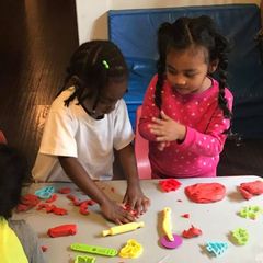 Two little girls are playing with play dough on a table.