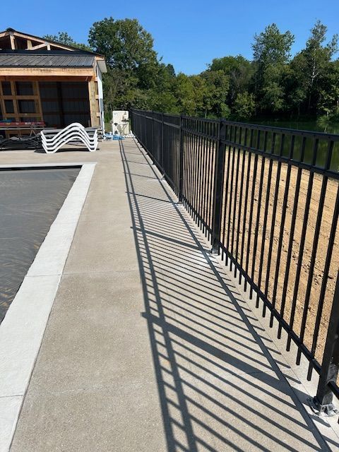 Black metal fence beside a concrete path, casting long shadows. River and trees in background.