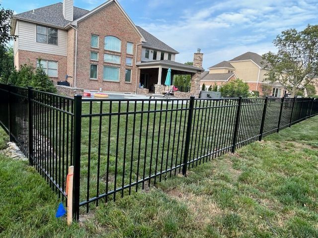Black metal fence surrounding a green grassy yard, with a large brick house in the background.