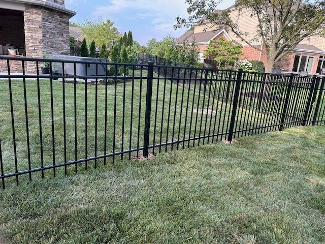 Black metal fence in a grassy yard, separating properties.