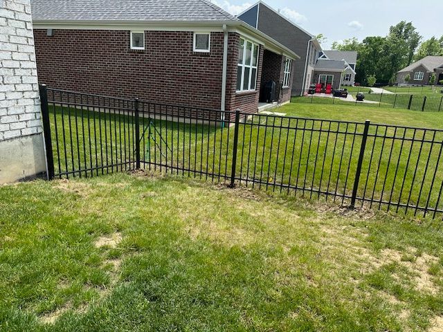 Black metal fence encloses a grassy backyard next to a brick house.