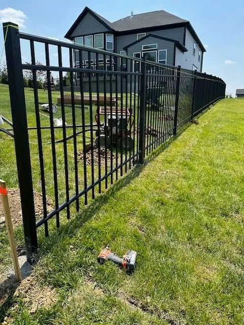 Black metal fence surrounding a green lawn, with a house in the background and a tool in the grass.