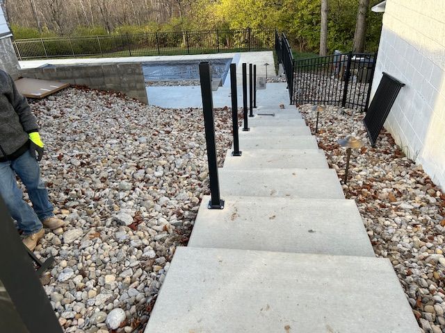 Concrete steps with black railing leading down to a pool area; a person on the side.