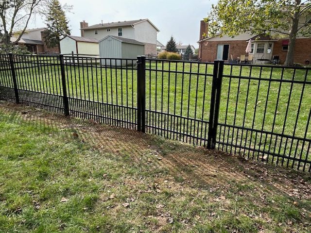 Black metal fence surrounding a grassy yard with houses in the background on a sunny day.