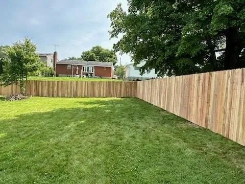 Wooden fence encloses a green lawn, with houses and trees visible in the background under a blue sky.