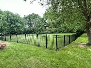 Black metal fence encloses a green lawn, surrounded by trees.
