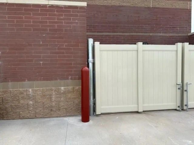 Tan vinyl gate against a red brick building, red bollard next to the gate.