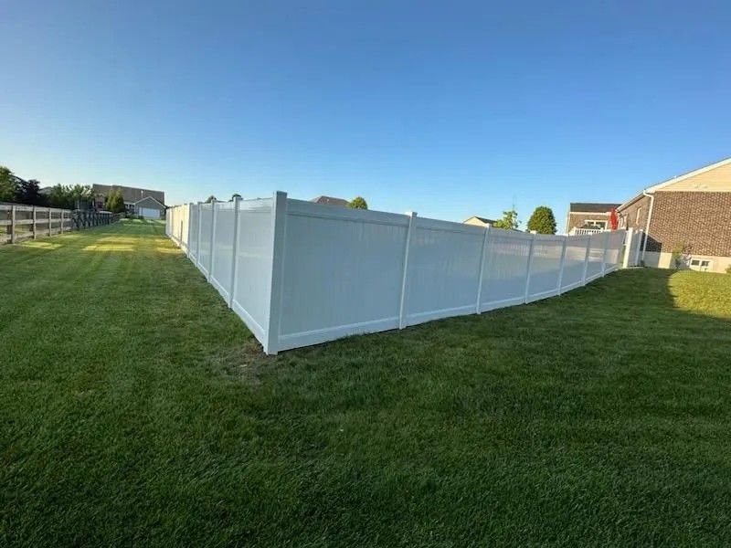 White vinyl fence enclosing a green lawn on a sunny day.