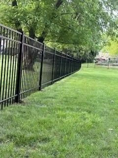 Black metal fence along a grassy lawn, trees in background.
