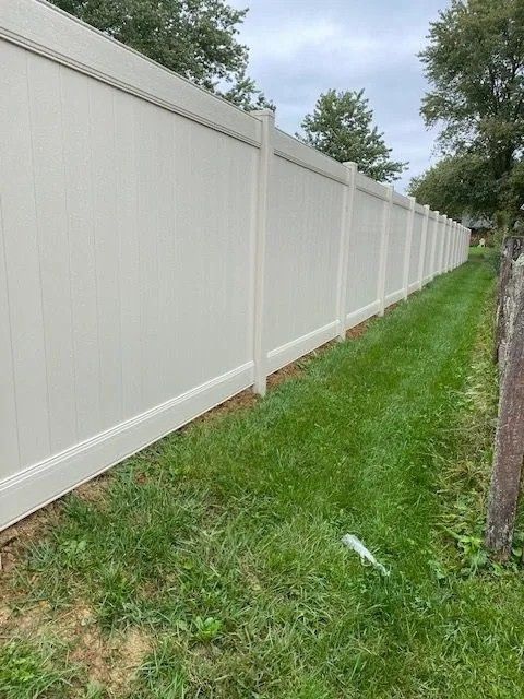 Beige vinyl fence along a grassy yard, under a cloudy sky.