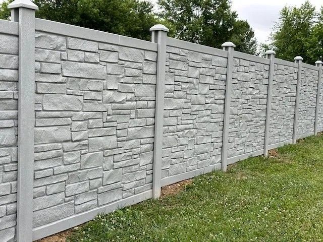 Gray concrete fence with a stone texture, in a grassy area.