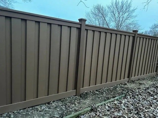 Brown vinyl privacy fence outdoors with vertical panels and decorative posts.