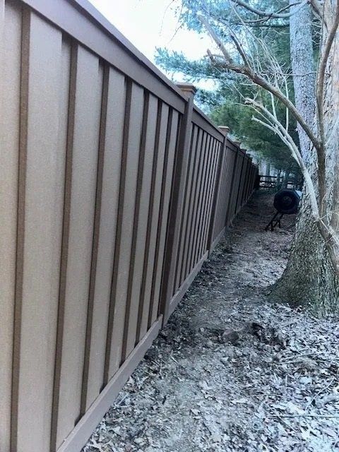 Brown vertical fence along a dirt path next to trees.