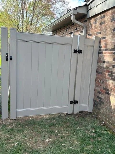Tan vinyl gate next to a brick wall and gutter, grass below.