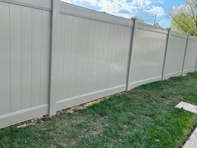 Tan vinyl privacy fence in a grassy yard under a blue sky.
