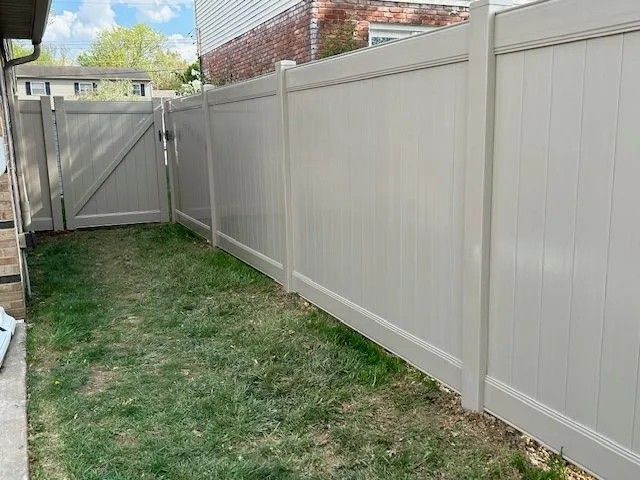 Tan vinyl fence enclosing a grassy yard with a gate, adjacent to a brick house.