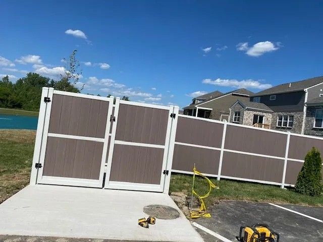 Brown and white vinyl fence and gate against a blue sky, cement pad, and adjacent grass.