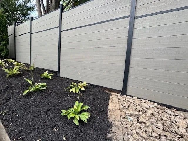 Gray composite fence with black posts, bordering a garden bed of dark mulch and plants.
