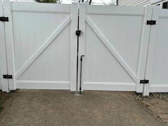 White vinyl gate with black hardware; angled cross braces; concrete ground.