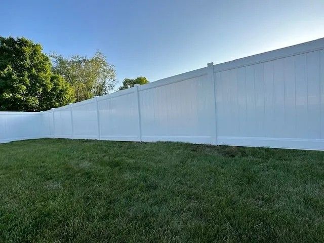 White vinyl privacy fence in a grassy yard under a blue sky.