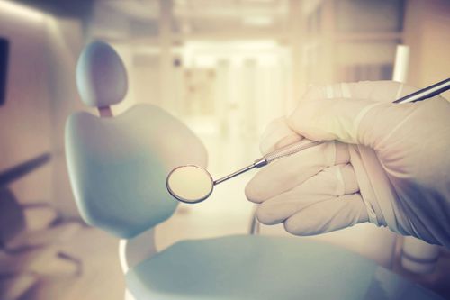 Gloved hand holding a dental mirror near a chair in a bright clinic