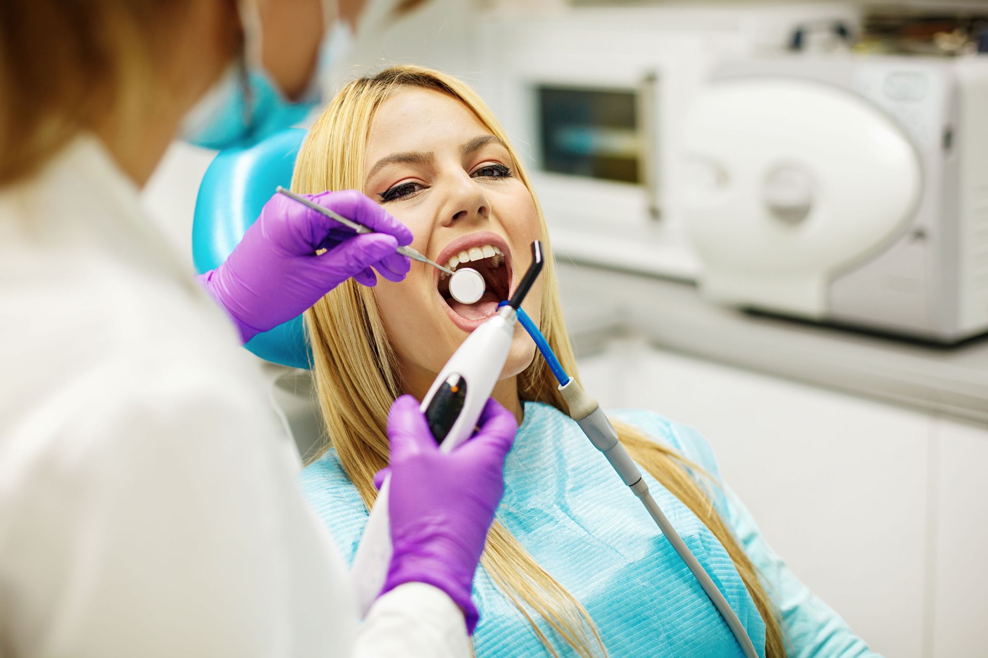 Dentist examining a patient in a dental chair, using purple gloves and a handheld tool.