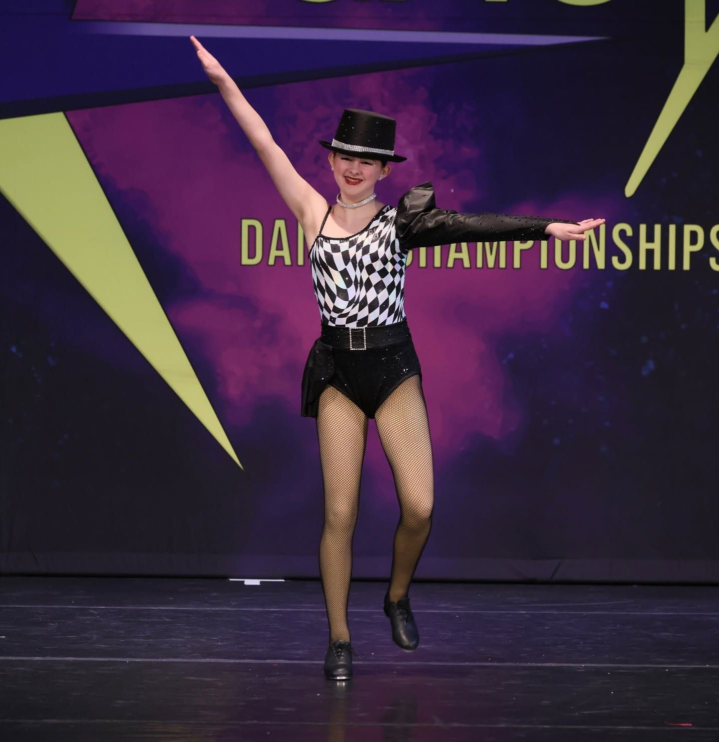 Dancer in black-and-white costume and hat performing on stage at dance championships