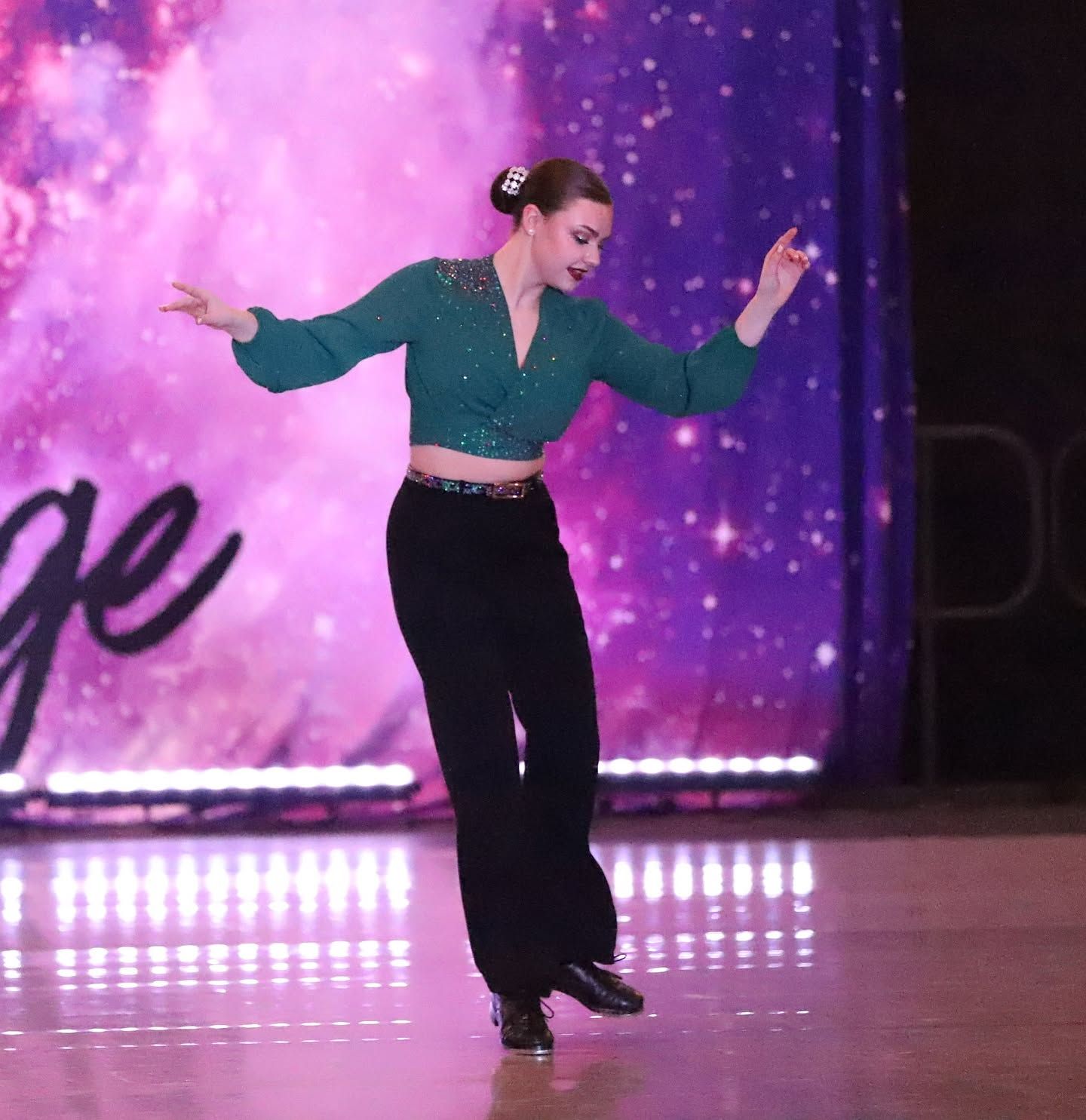Dancer in teal top and black pants posing onstage against a purple starry backdrop