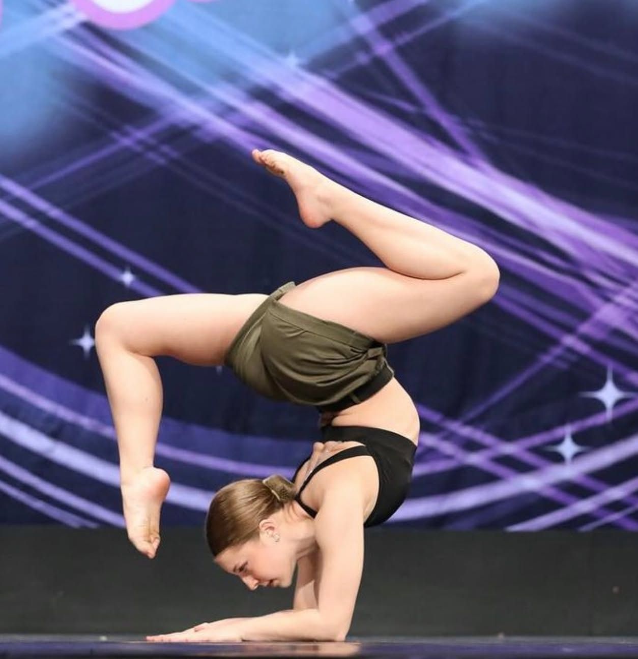 Contortionist balancing on one arm in a dramatic stage performance with purple light beams