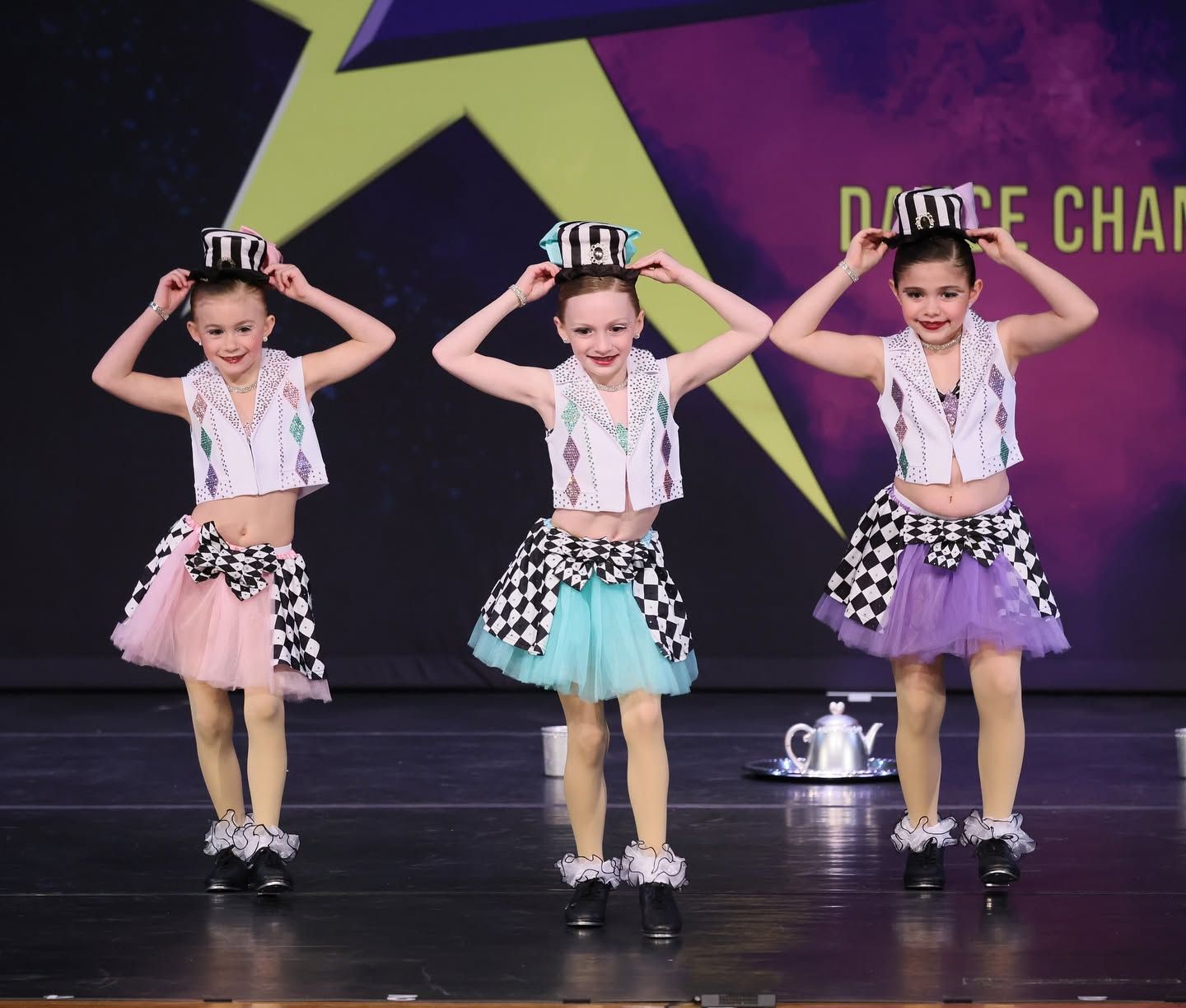 Three young dancers in colorful costumes posing onstage with hands on their hats