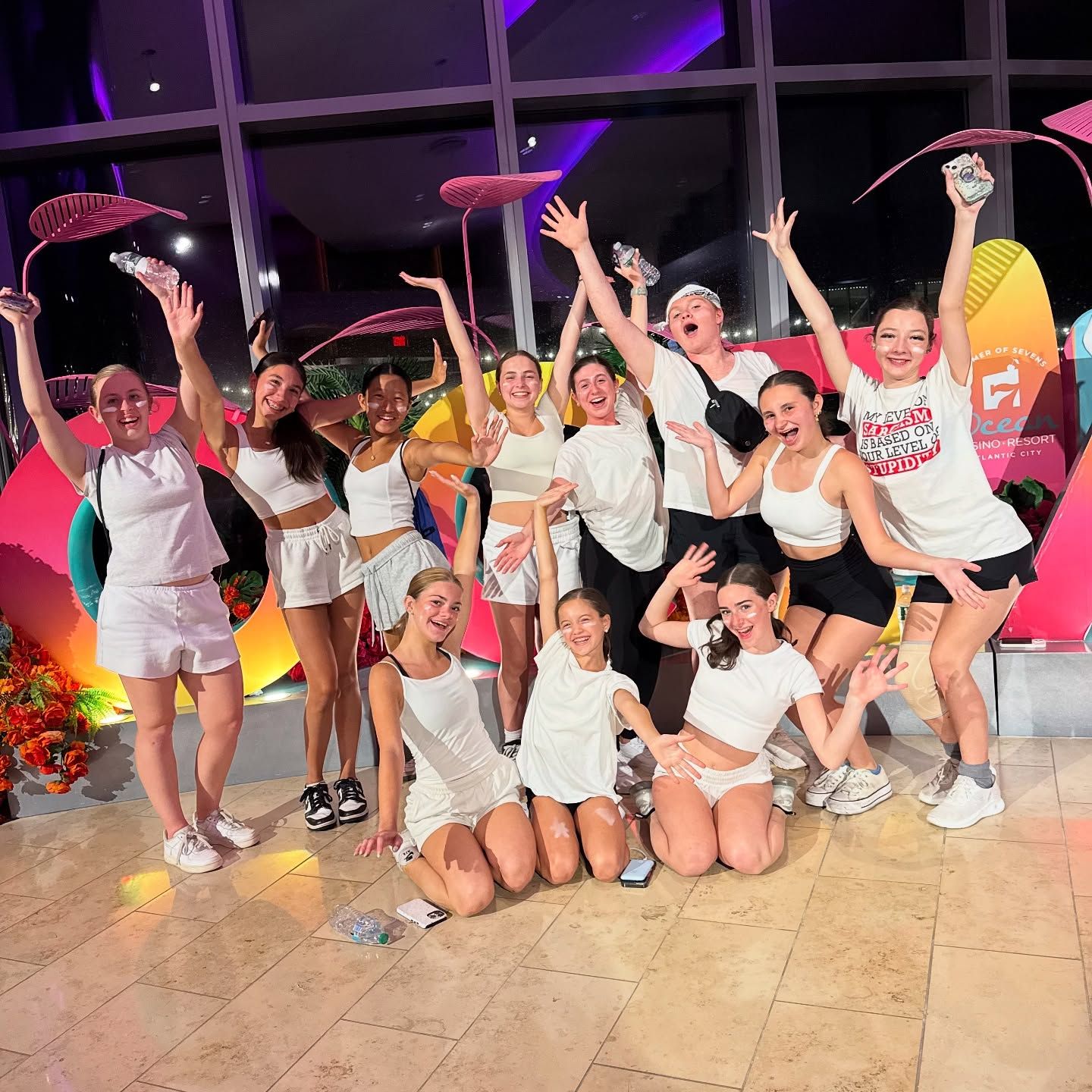 Group in white outfits posing and cheering under pink umbrellas at a nighttime event.