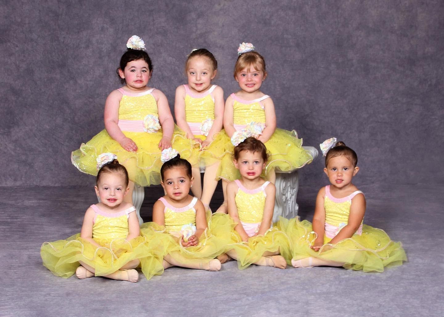 Six children in yellow tutus pose against a gray studio backdrop.