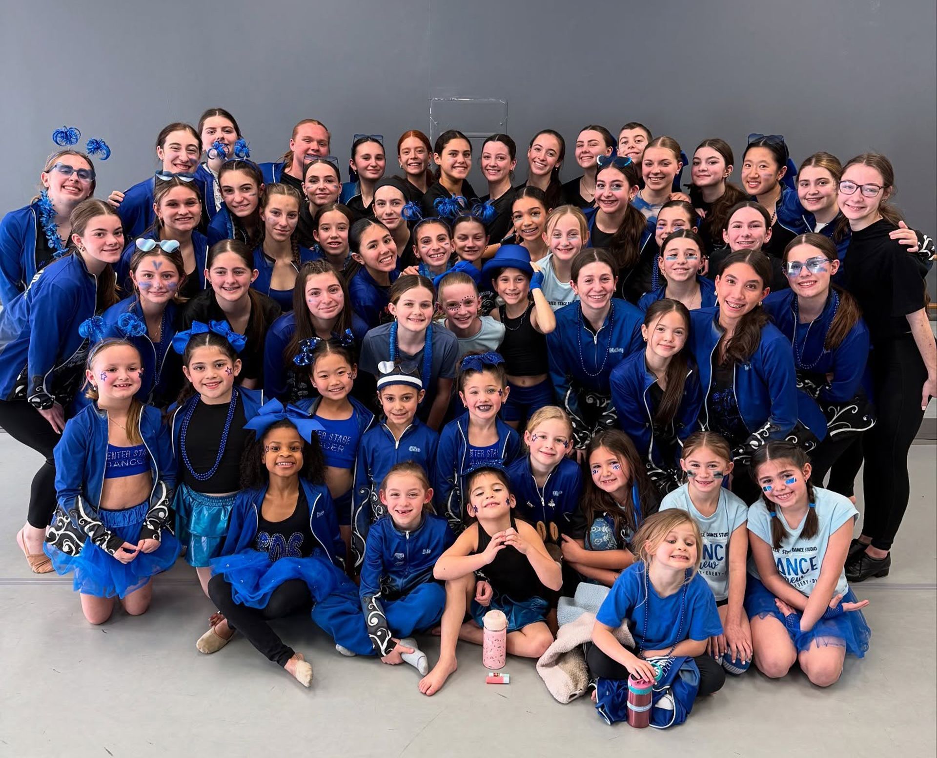Large group posing indoors in matching blue outfits, smiling at the camera.