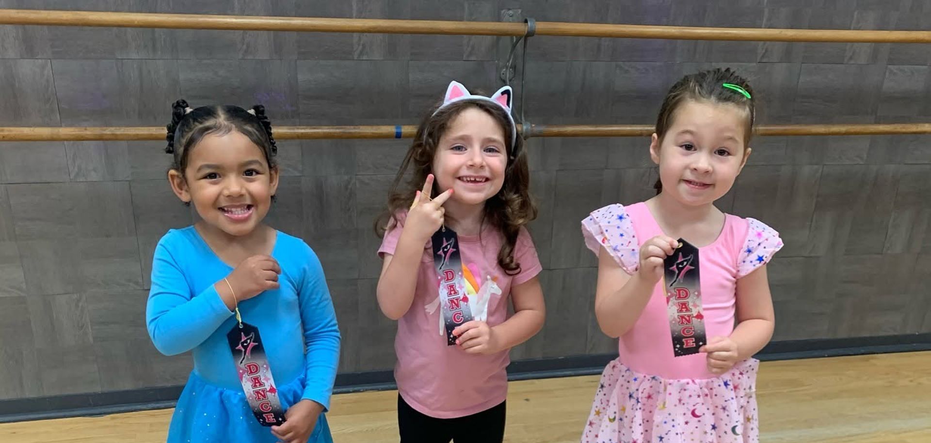 Three children smiling and posing with peace signs in front of a gym wall