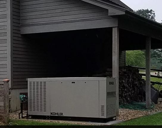A large Kohler generator is sitting under a porch next to a house.