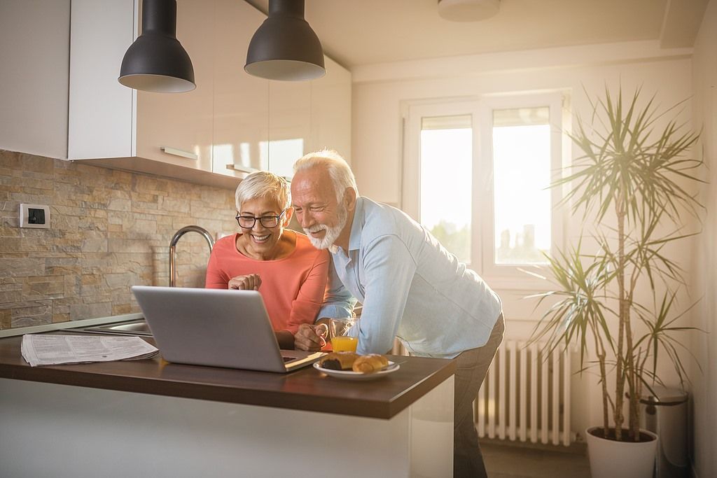 An elderly couple is using a laptop computer in the kitchen.