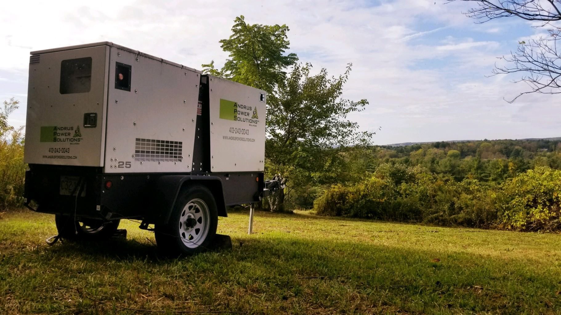 A generator is parked in a grassy field with trees in the background.
