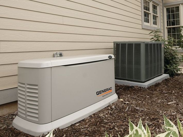 A generator is sitting next to an air conditioner on the side of a house.