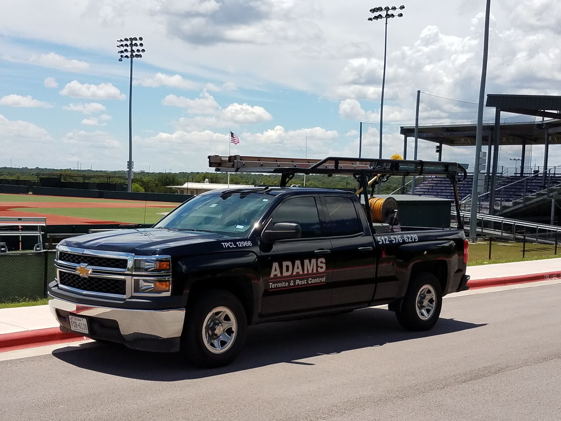 Black work truck with equipment rack parked by a baseball field. 
