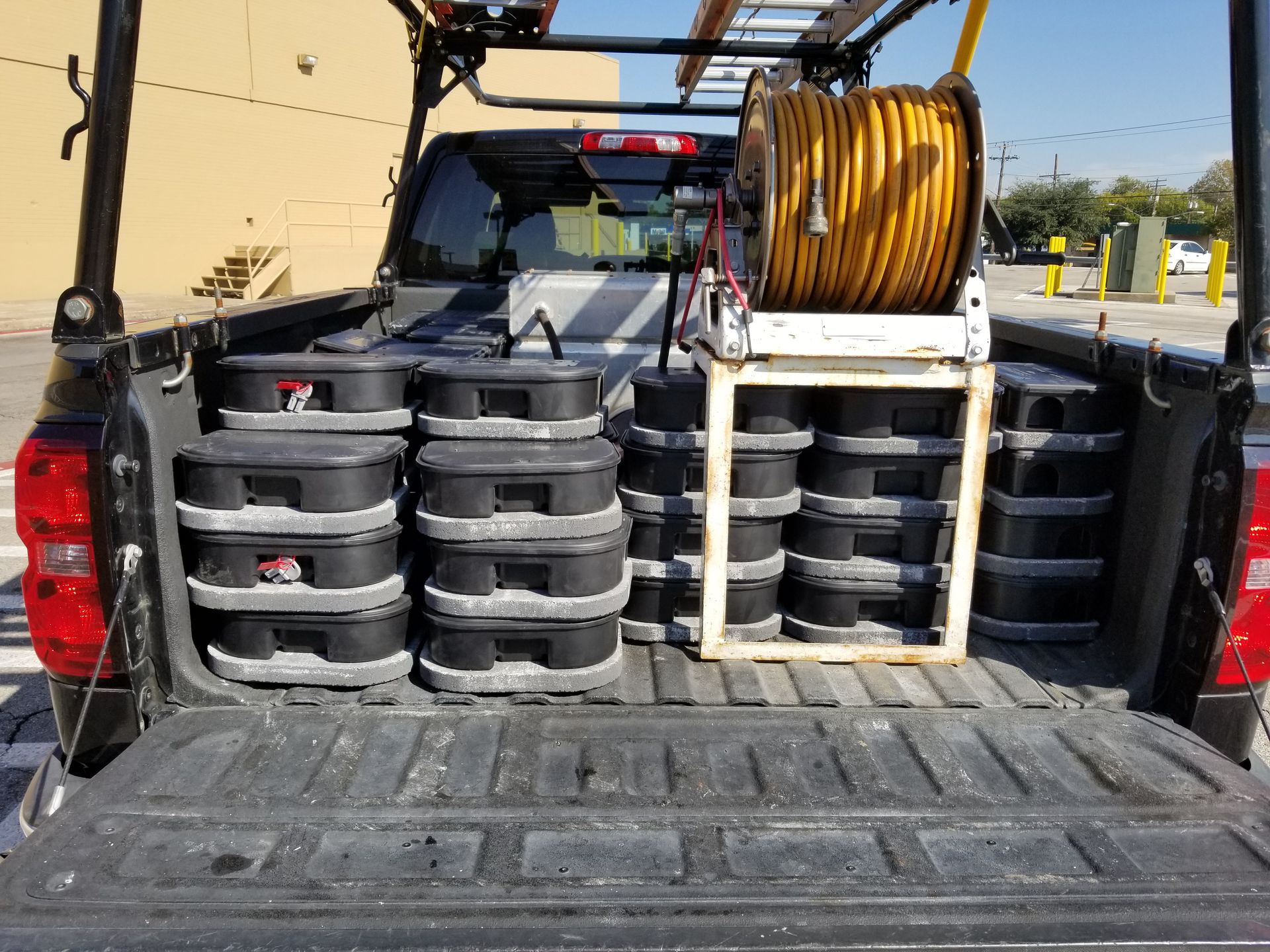 Truck bed loaded with stacks of black toolboxes and a yellow extension cord on a reel.