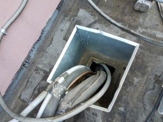 Electrical cables bundled inside a metal box recessed in concrete.