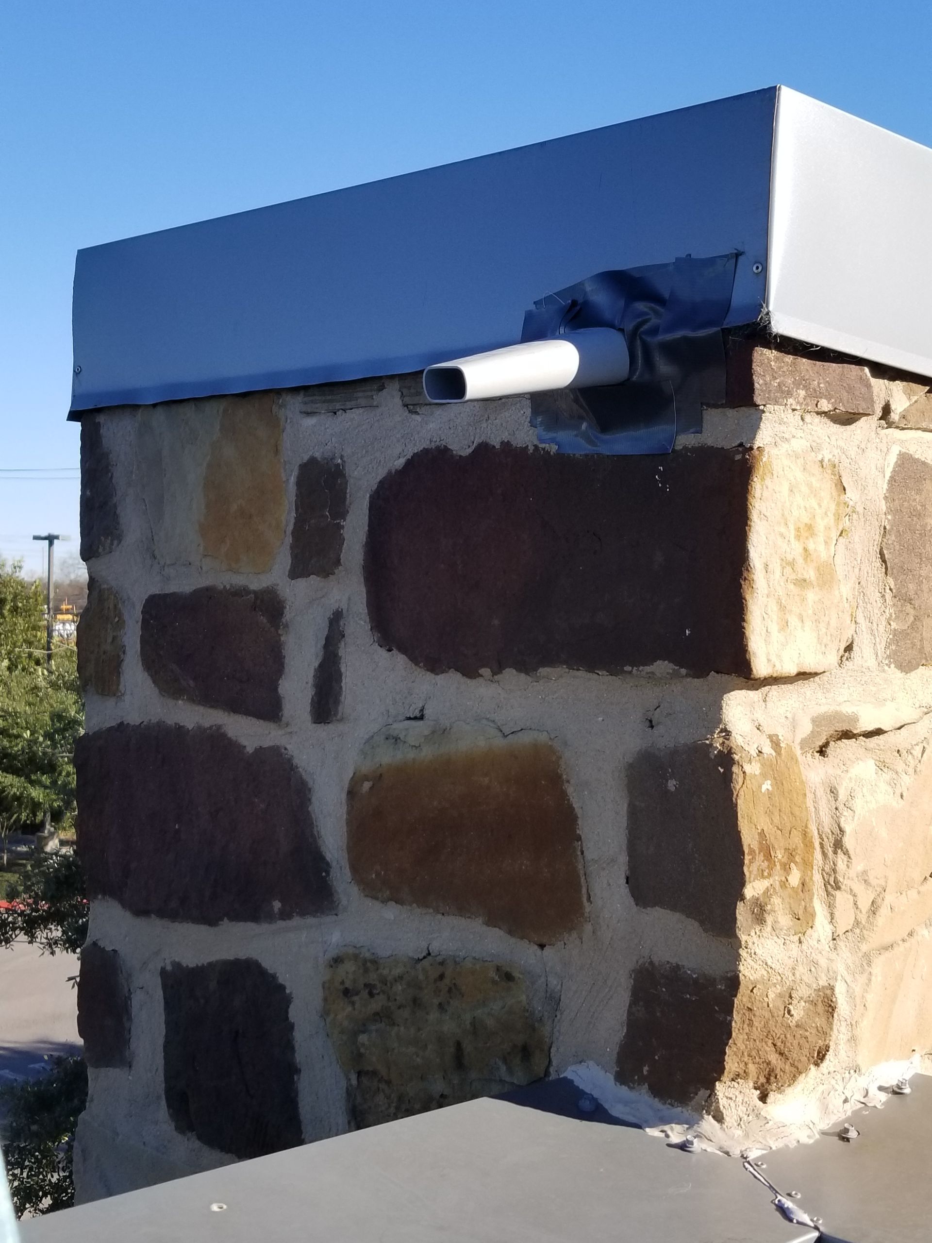 Stone chimney with gray metal cap and a white pipe.