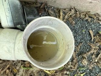 Open PVC pipe with standing, murky water. Close up shot with black gravel and leaves visible.