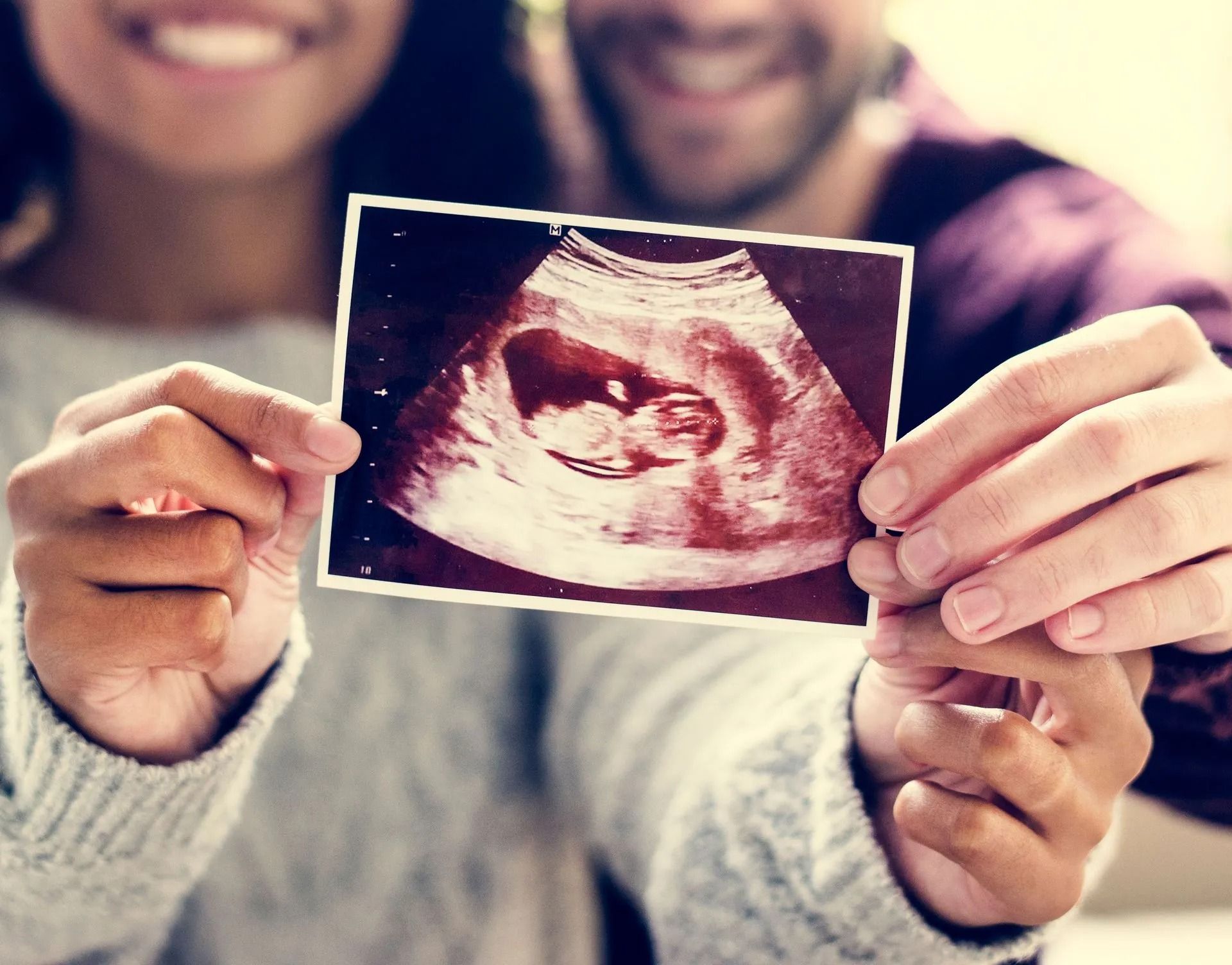 Couple holding an ultrasound photo of a fetus, smiling.