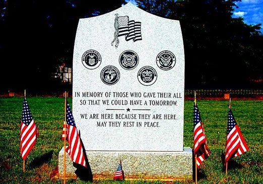 A gravestone in a cemetery with american flags in front of it.