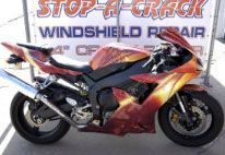 A red and yellow motorcycle is parked in front of a sign for windshield repair.