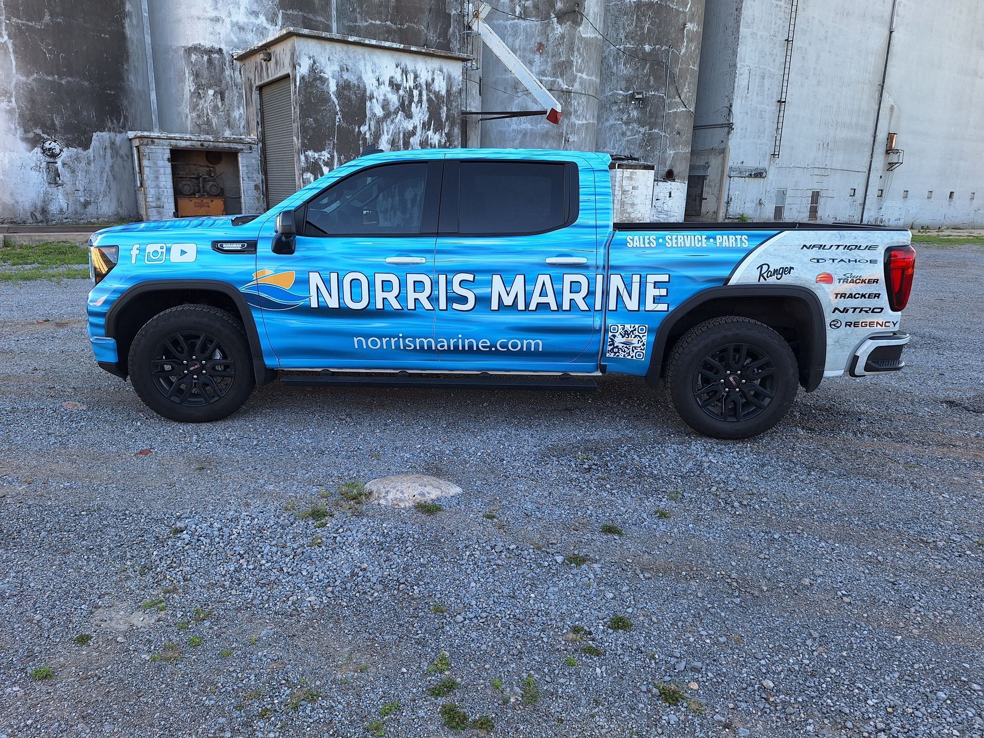 A blue truck with the word norris marine on the side is parked in a gravel lot.