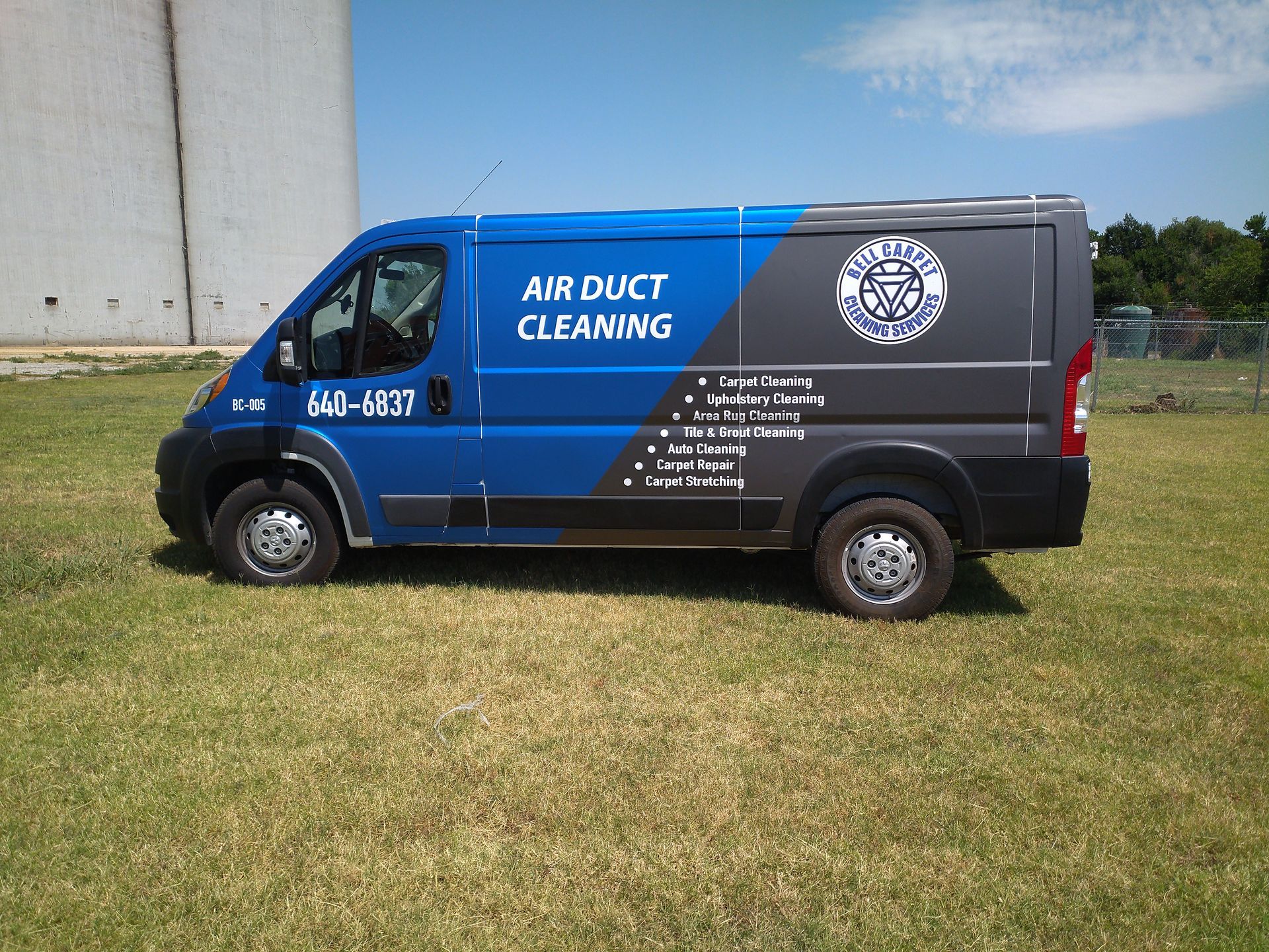 A blue and black van for air duct cleaning is parked in a grassy field.